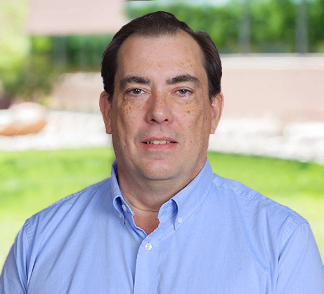 Headshot of John, a middle-aged man with short dark hair and a light complexion, wearing a light blue button-down shirt.
