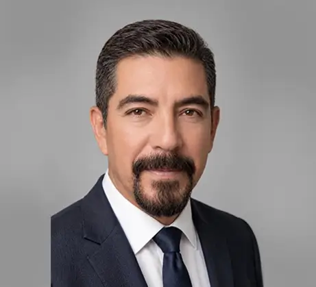 Headshot of Raul Treto, a man with short dark hair, brown eyes, and a goatee, wearing a suit jacket, white dress shirt, and dark tie against a grey background.